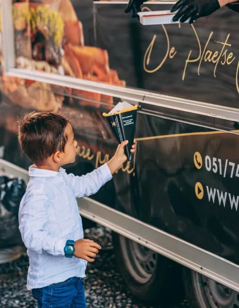 Jongen neemt een puntzak frietjes aan bij de mobiele frituur